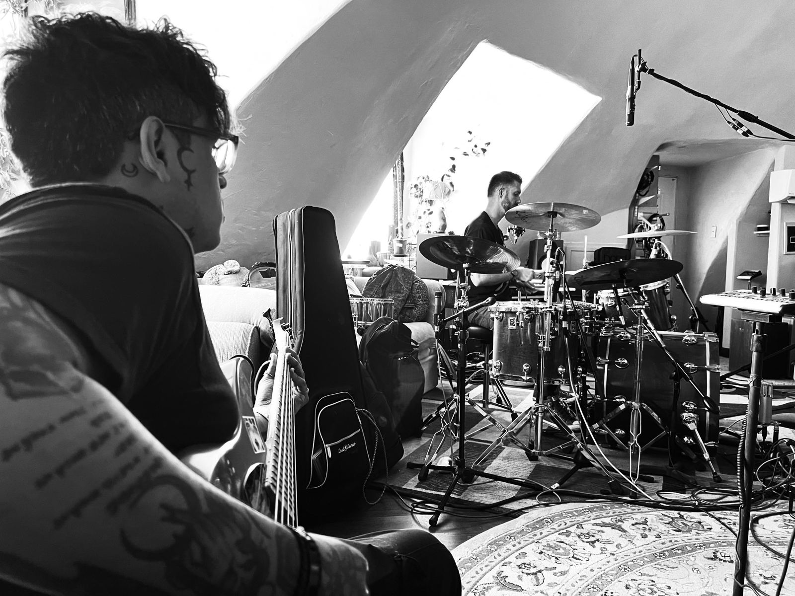 Black and white photo of musicians tracking live — guitarist and drummer under the dome skylight